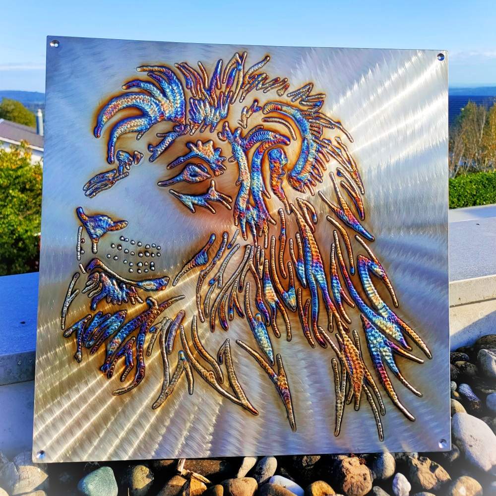 Welded lion face artwork on brushed metal with vibrant rainbow patina and textured detail